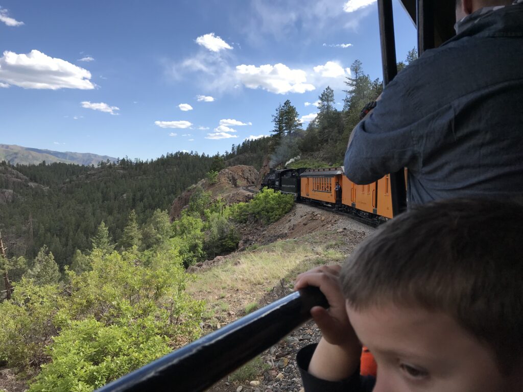 a boy looking out from a train, a view of the train engine on a forested mountain