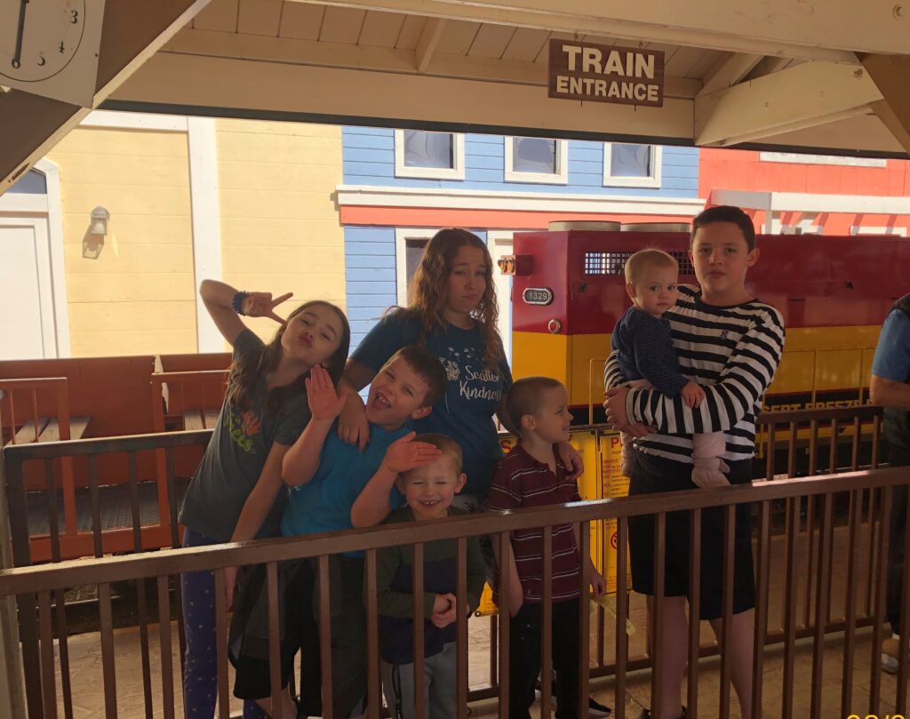 7 children in front of a small train, a "train entrance" sign