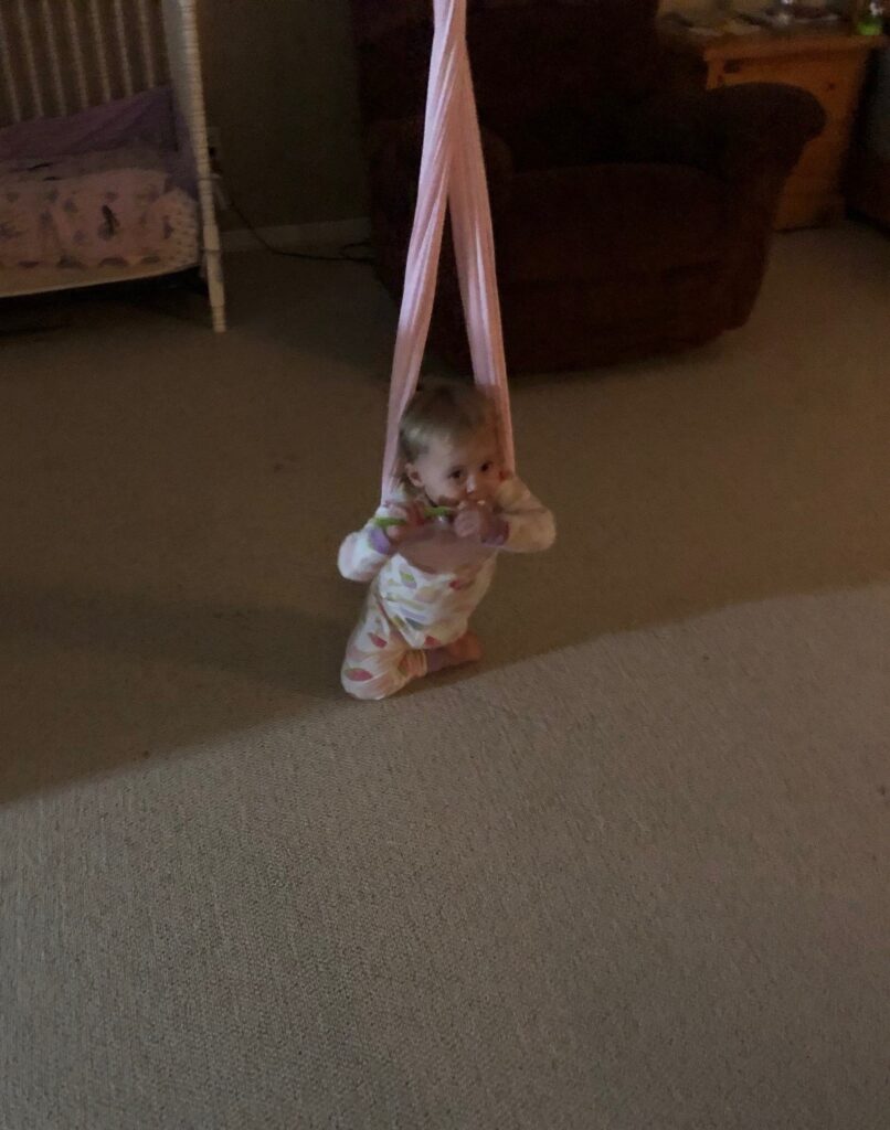 a toddler girl leaning on a hammock swing with her toothbrush