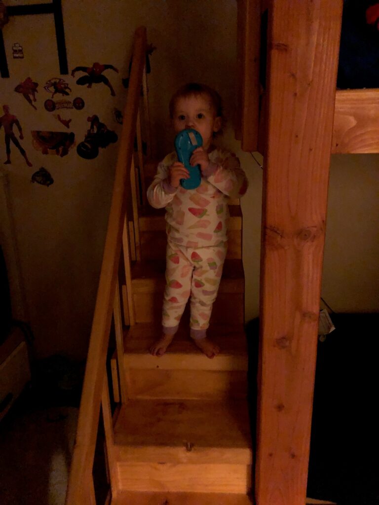 a toddler standing on bunkbed stairs holding a toy