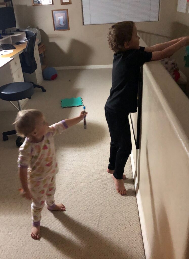 a toddler girl reaching a toothbrush to a boy