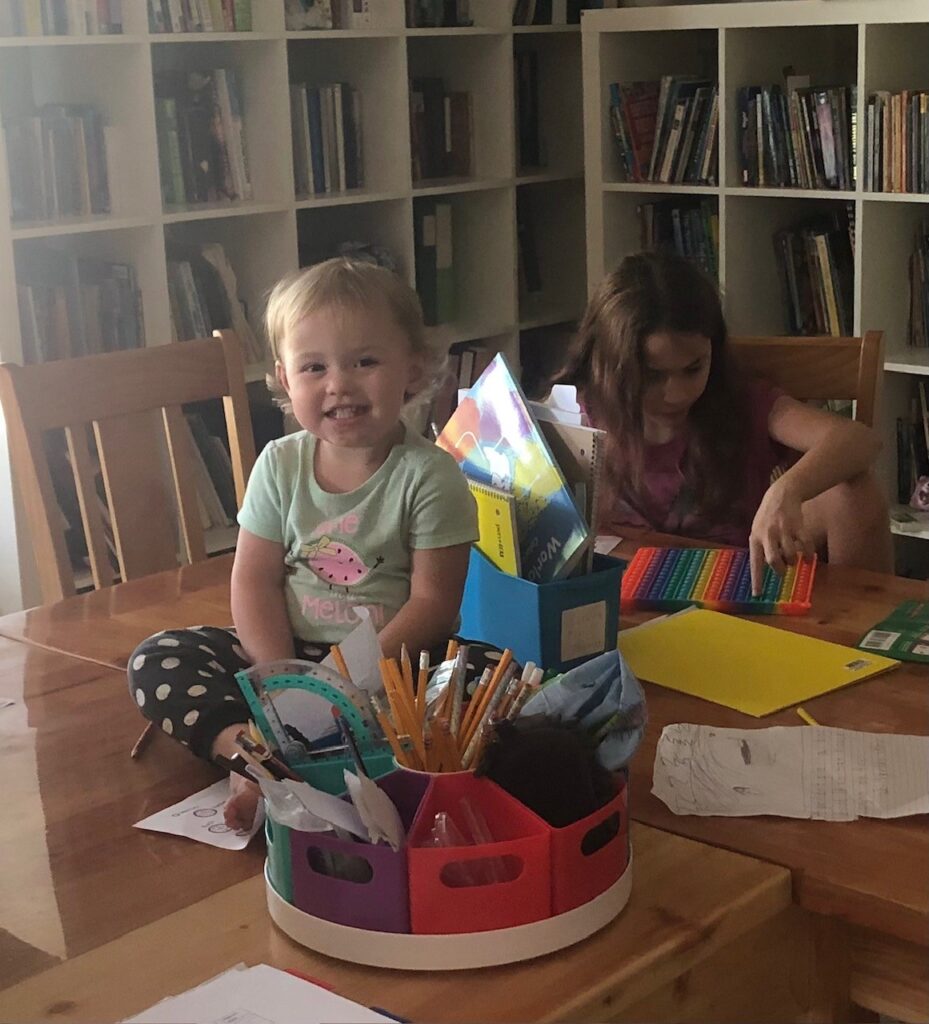 A toddler on the table with homeschool supplies