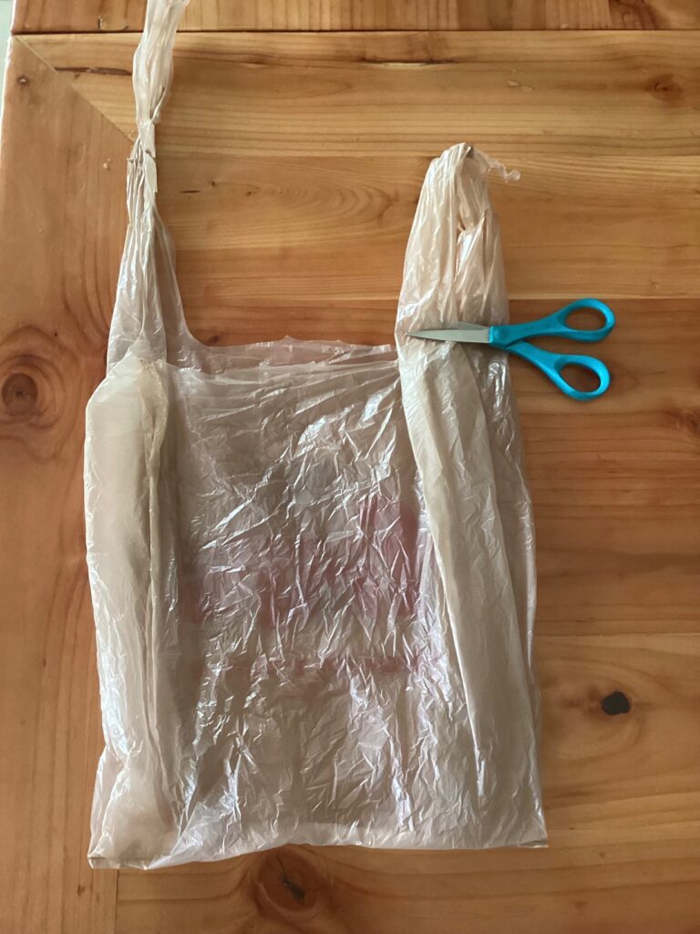 a plastic bag laid flat, scissors ready to cut the end of one handle, the other already cut