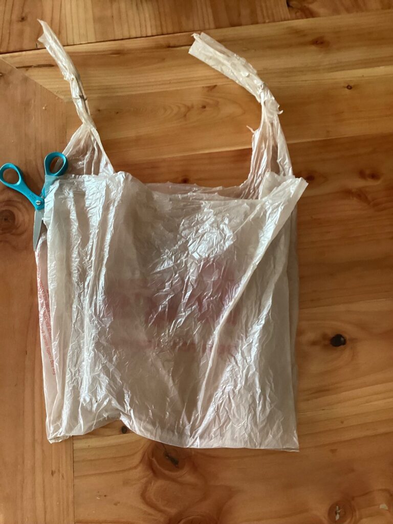 a plastic bag laid flat with one end of both handles cut and scissors ready to cut down the side