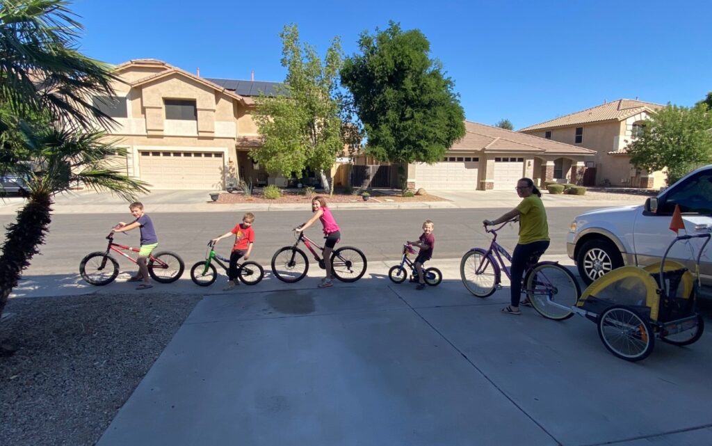 a woman on a bike with a trailer behind 4 children on bikes