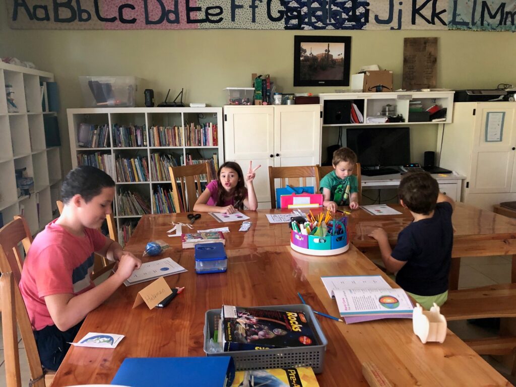 kids at a table doing school work, a bookshelf, computer, and wall alphabet in the background