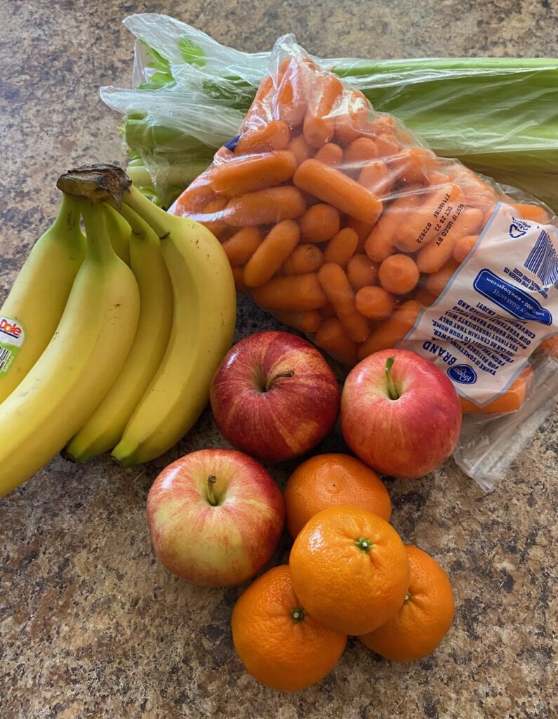 Celery, baby carrots, bananas, apples and oranges arranged on a counter