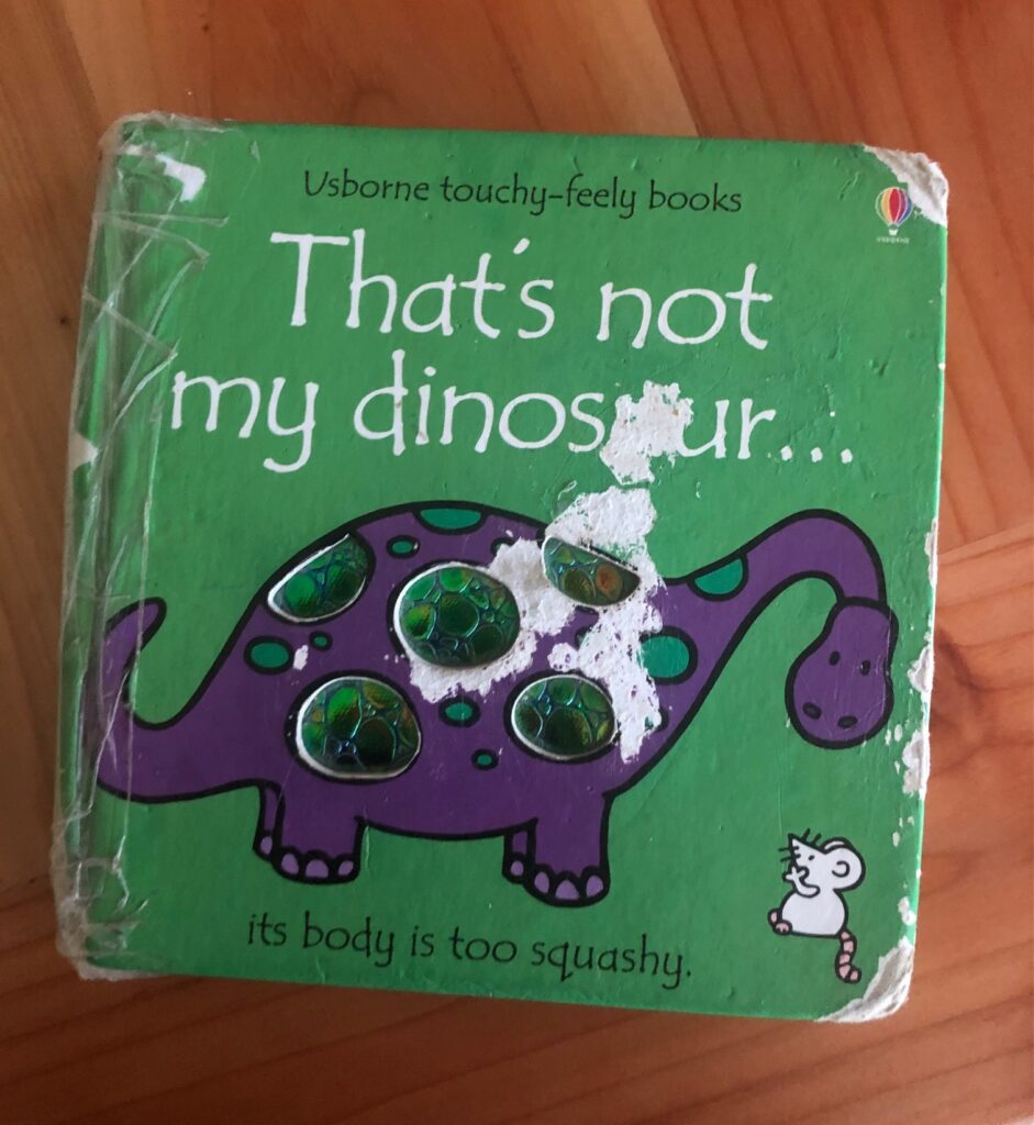 a well worn board book titled "That's not my dinosaur" with a purple dinosaur and a mouse on the cover