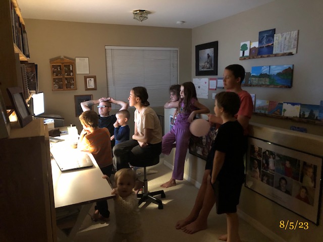 children of multiple ages gathered around a man and his computer