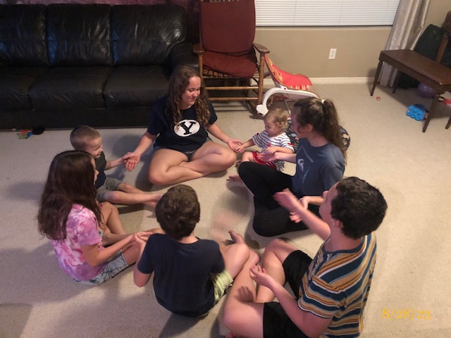 7 kids sitting together on the floor playing a hand game