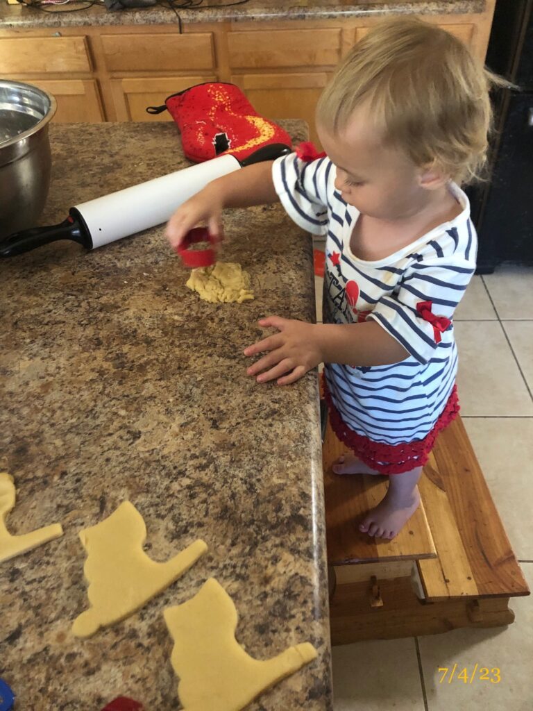 a toddler girl standing at a counter with dough and a cookie cutter