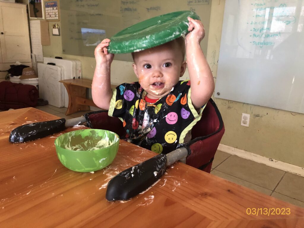 an older baby with food on her face and an upside down plate on her head