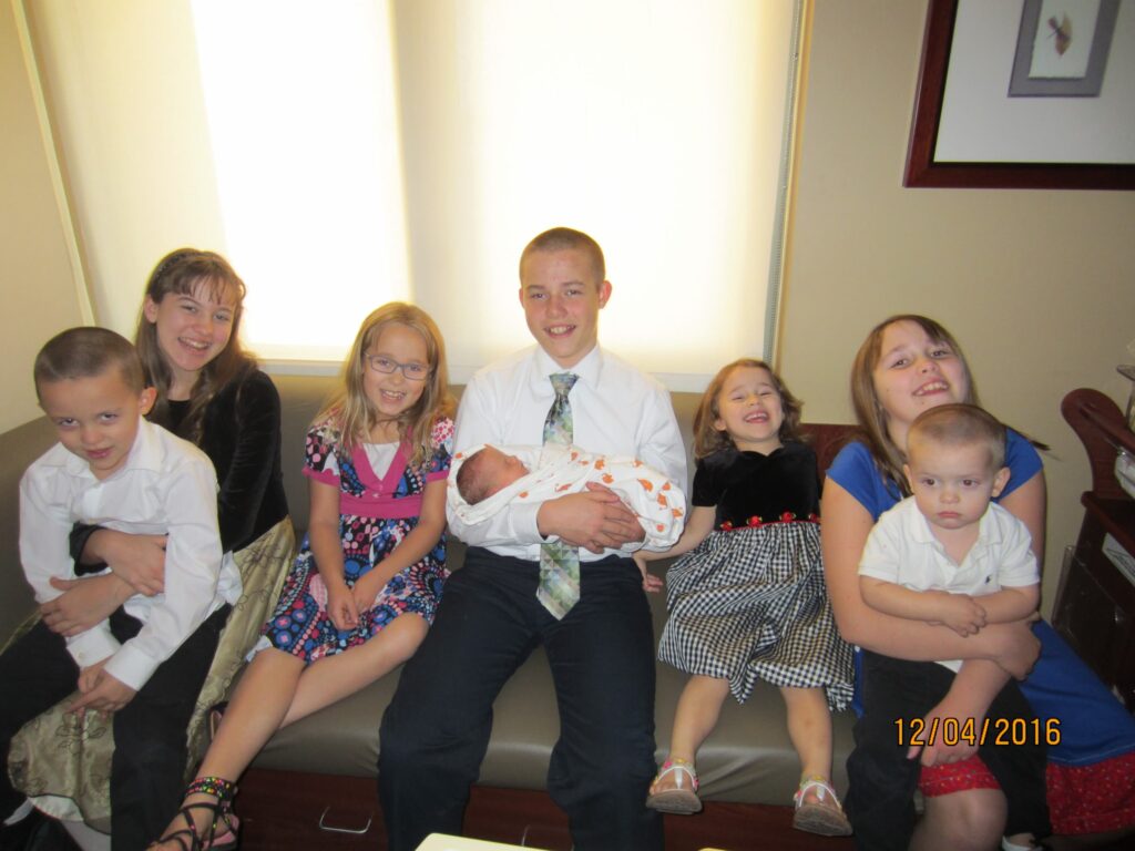 8 children gathered on a sofa, the oldest in the middle holding the newest baby