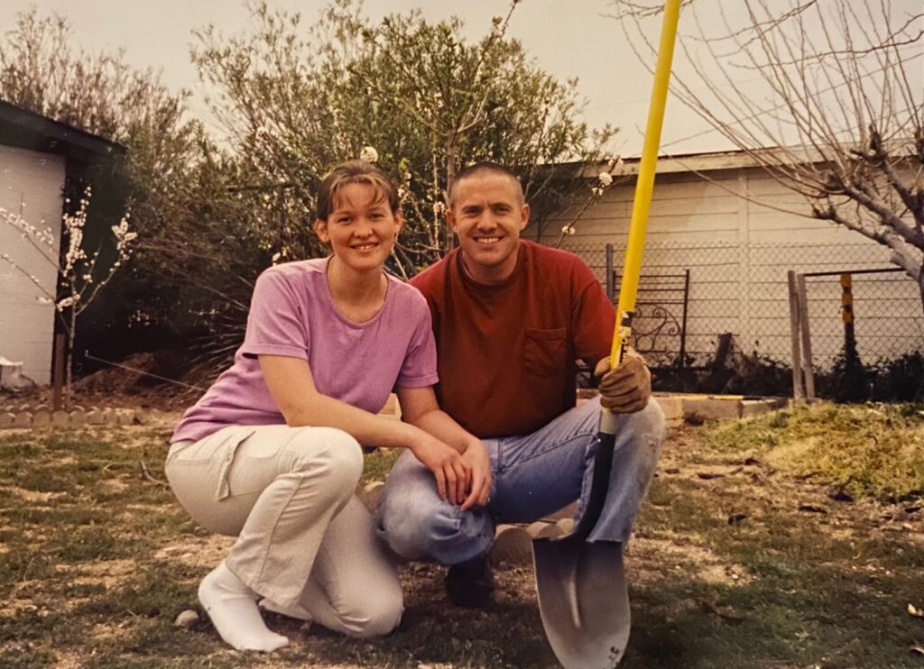 a young man and woman crouching together in front of their blossoming young fruit trees