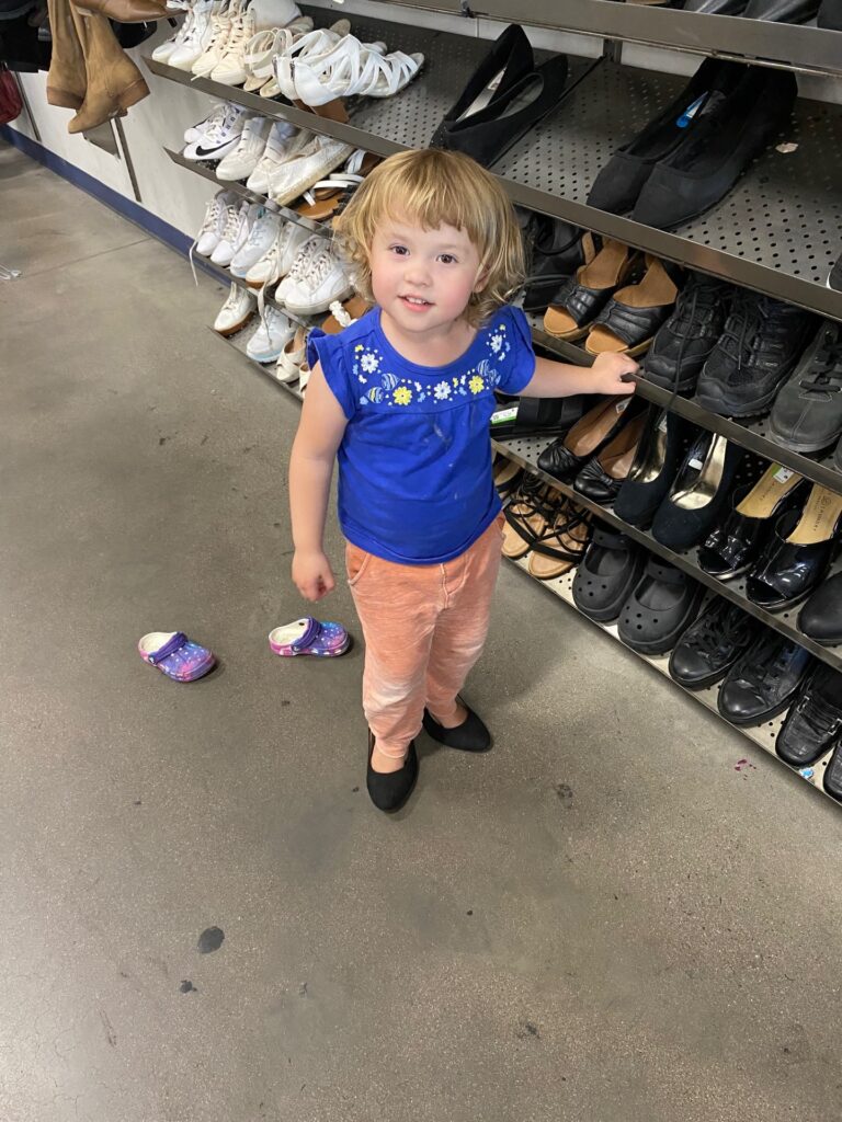 A 2 year old girl trying on women's shoes at a store