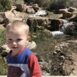 a toddler boy walking past a small waterfall