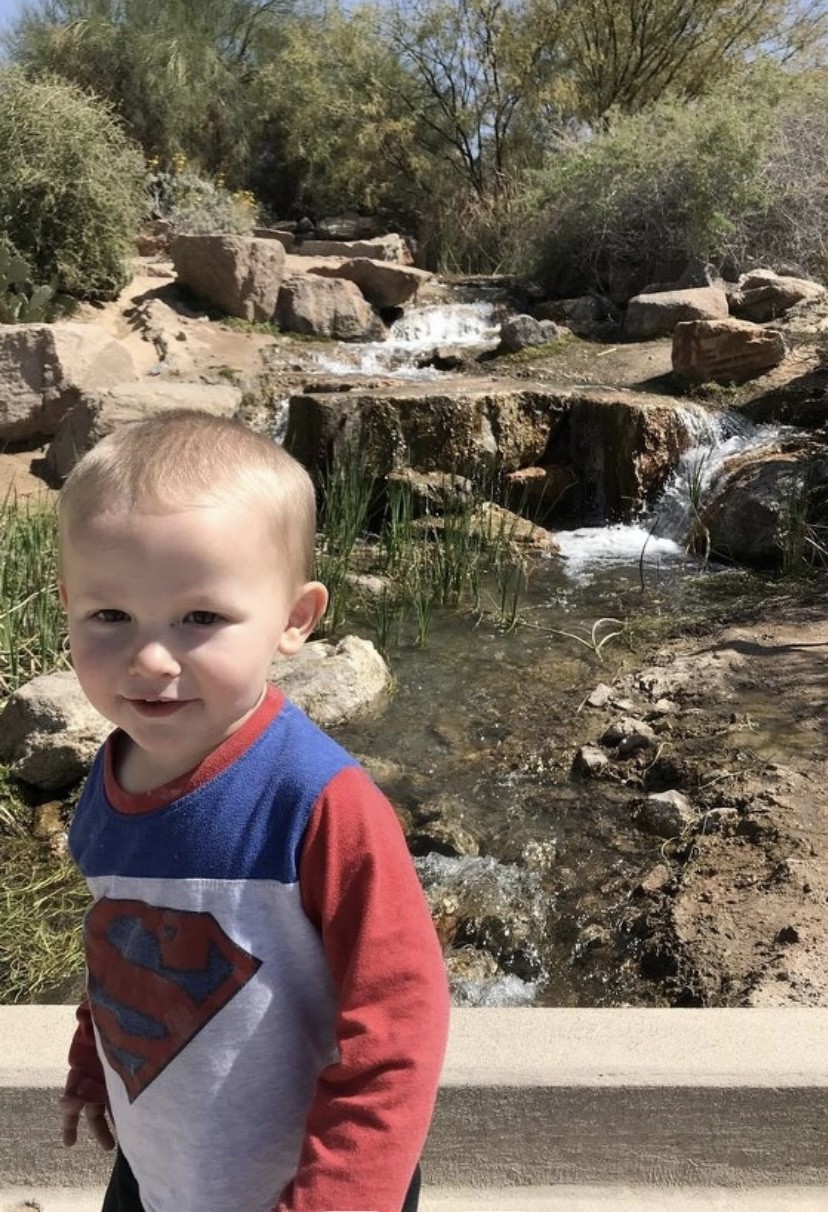 a toddler boy walking past a small waterfall