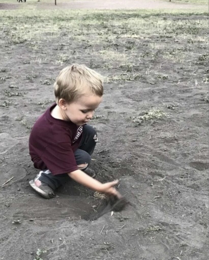 a 2 year old boy squatting down to feel the dirt