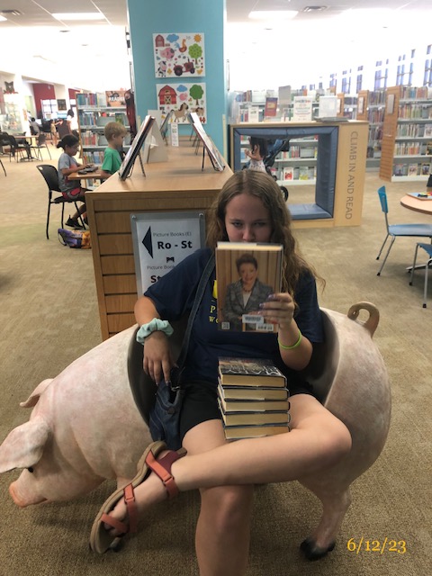 a girl in the library with a stack of books in her lap