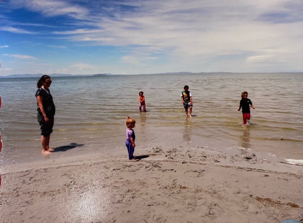 A pregnant woman watching her kids at a beach