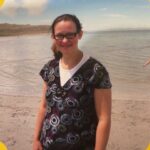 A pregnant woman standing on a beach smiling