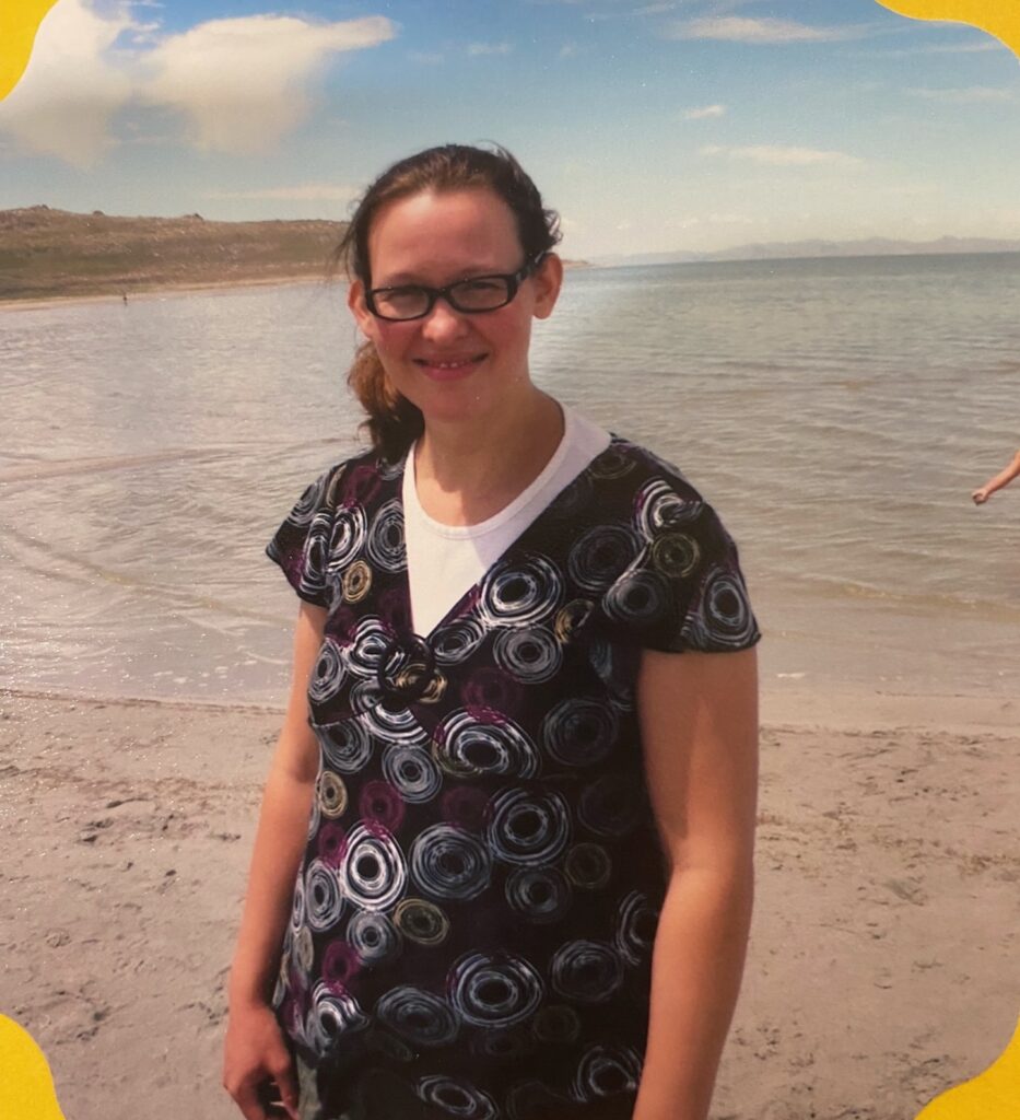 A pregnant woman standing on a beach smiling