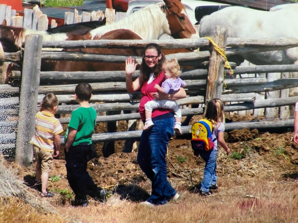 A pregnant lady waving at the camera, a little girl on her hip