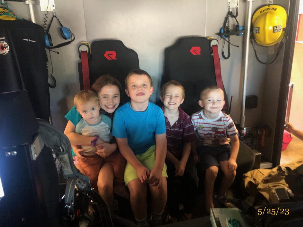 Five kids smiling in the cab of a fire engine