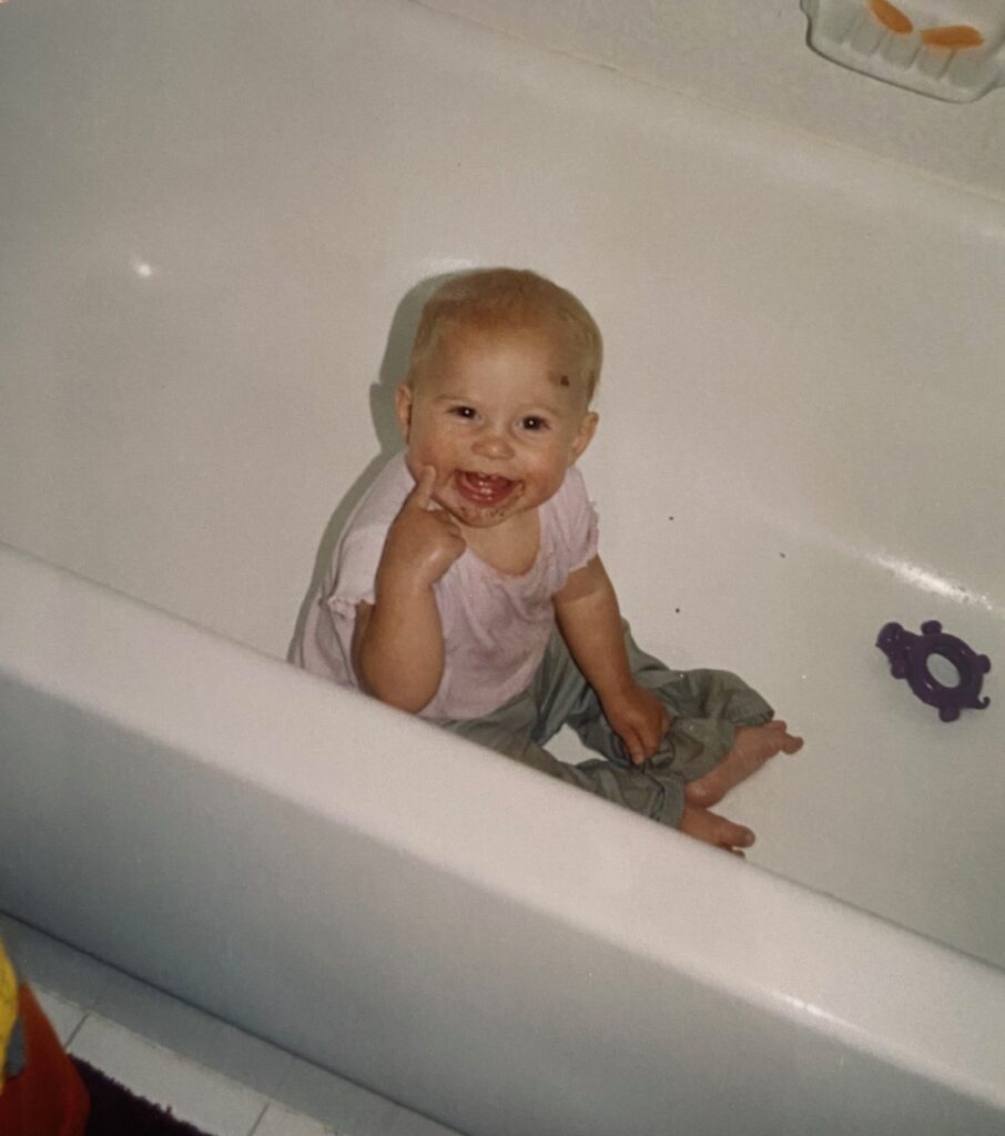 dirty clothed baby smiling in empty bathtub